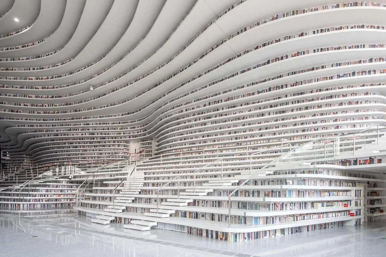 Biblioteca com estantes brancas que se curvam como páginas de um livro